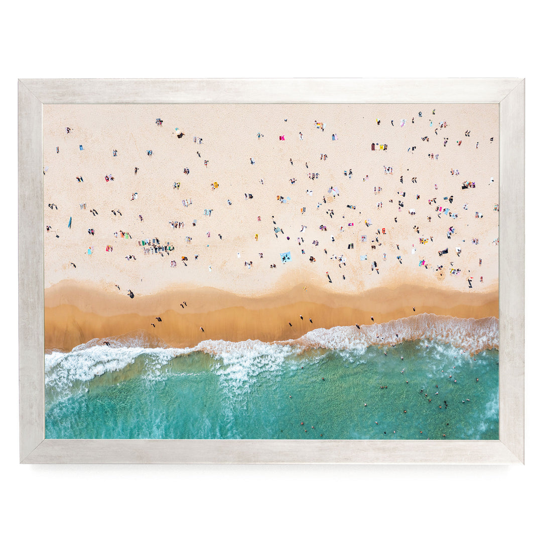 a crowded beach with numerous people enjoying the sunny day, the waves crashing onto the shore, and the sky above filled with clouds.