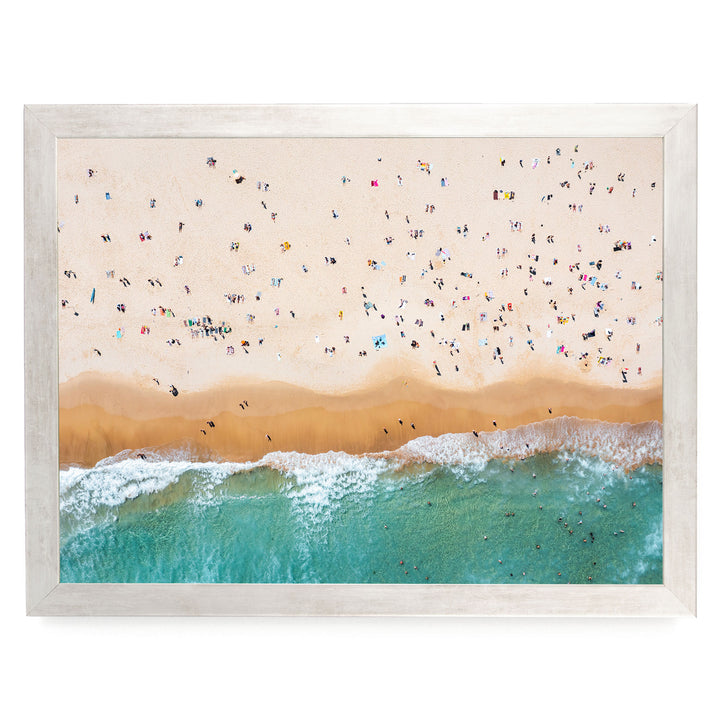 a crowded beach with numerous people enjoying the sunny day, the waves crashing onto the shore, and the sky above filled with clouds.