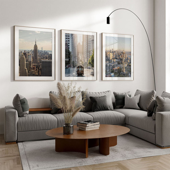 a modern living room with a gray sectional sofa, a wooden coffee table, and three framed cityscape photographs on the wall.