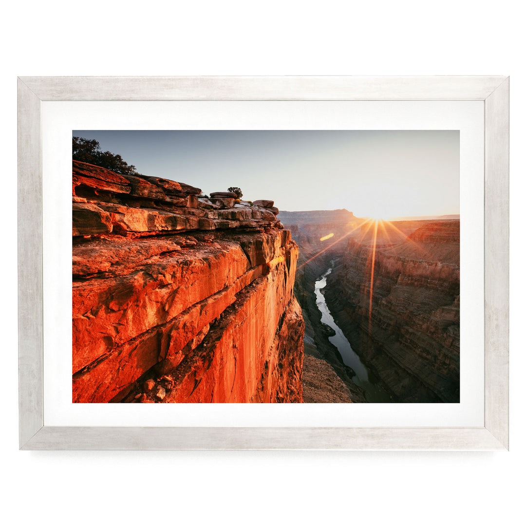 A framed photograph depicting a dramatic canyon landscape with a river flowing through it, set against a backdrop of a sunrise or sunset.