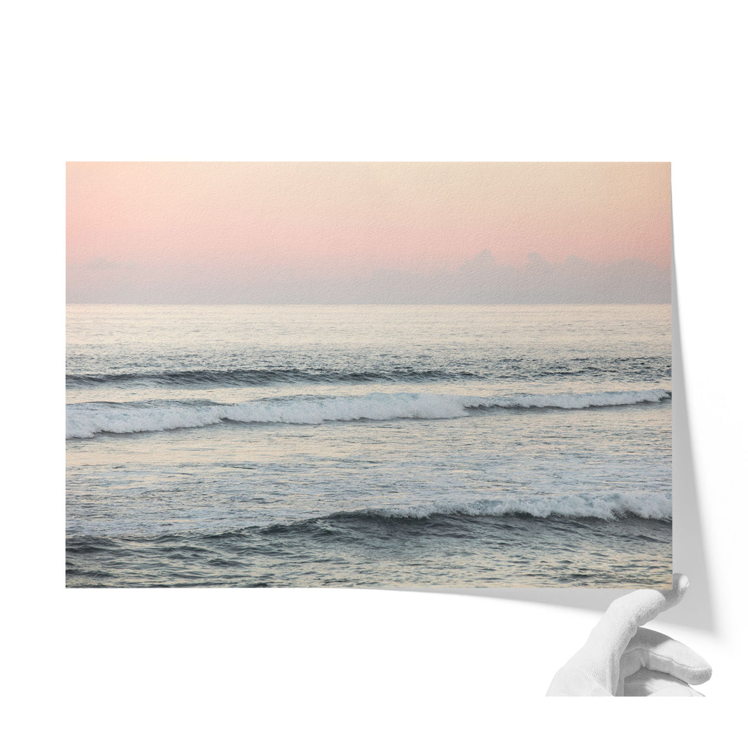 A hand is holding a piece of paper with a serene image of a sunset over the ocean, featuring waves crashing against the shore.