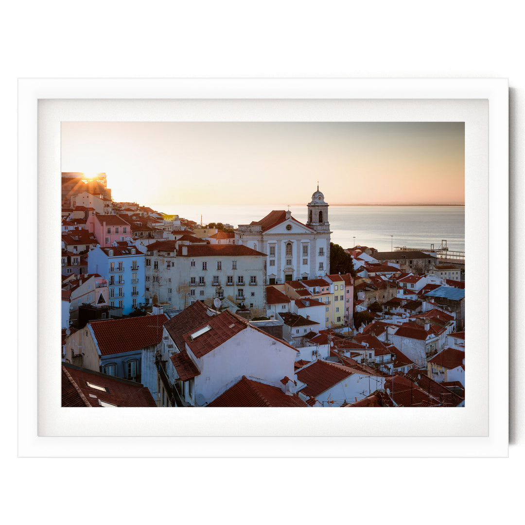 a picturesque town with a church and colorful buildings set against a backdrop of a sunset over the ocean.