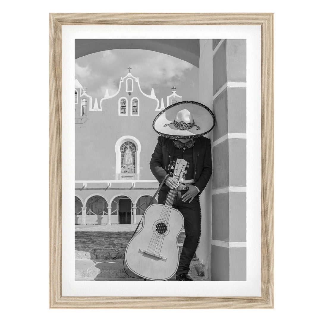 A person wearing a sombrero and holding a guitar stands in front of a building with arched windows.