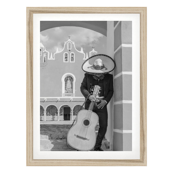 A person wearing a sombrero and holding a guitar stands in front of a building with arched windows.