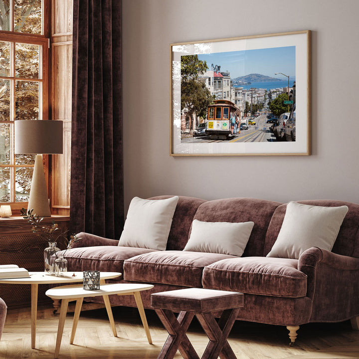 a cozy living room with a large window, a brown sofa, a coffee table, and a framed picture of a trolley car on the wall.