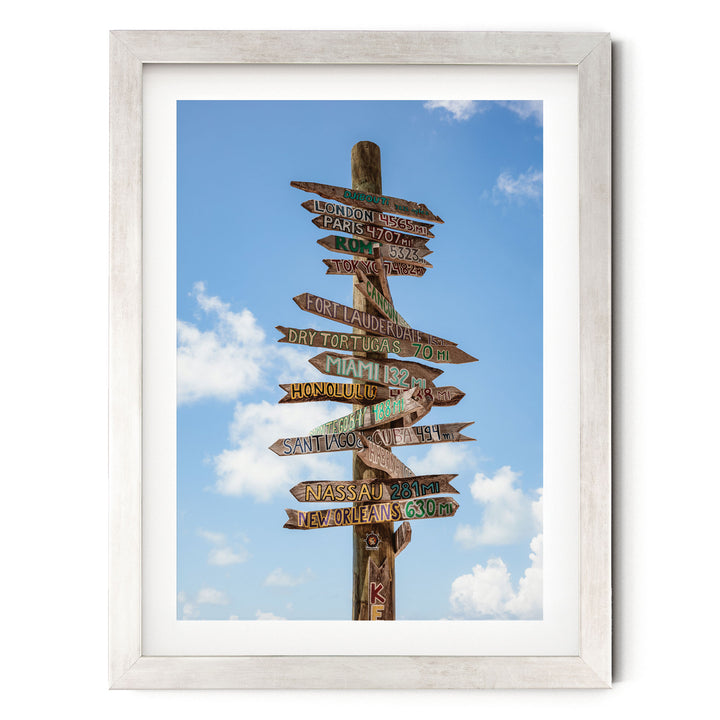 a wooden signpost with various destinations written on it, set against a blue sky with clouds.