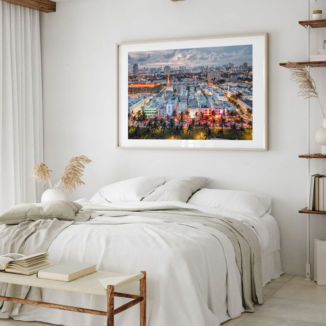 a bedroom with a large framed picture of a city skyline hanging on the wall above a bed with white linens and pillows.