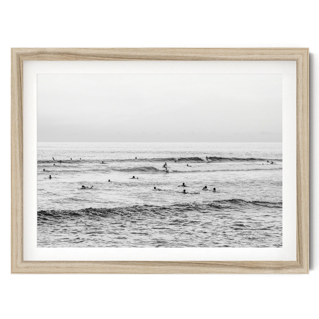 A black and white photograph of a group of people surfing in the ocean, with waves visible in the background.