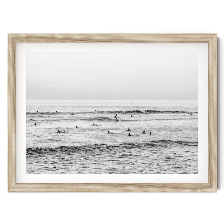A black and white photograph of a group of people surfing in the ocean, with waves visible in the background.