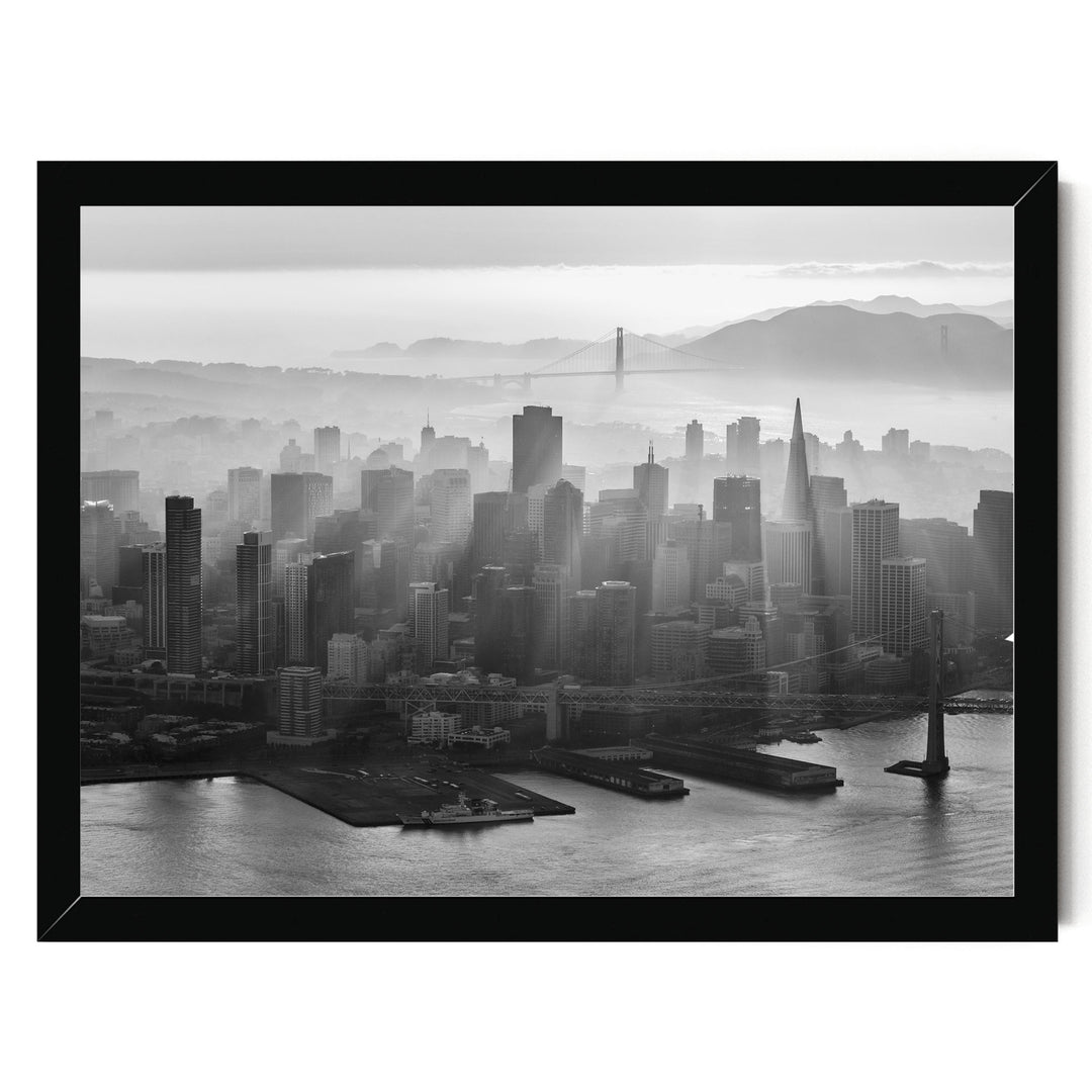A black and white aerial view of the San Francisco skyline, with the Golden Gate Bridge and foggy mountains in the background.