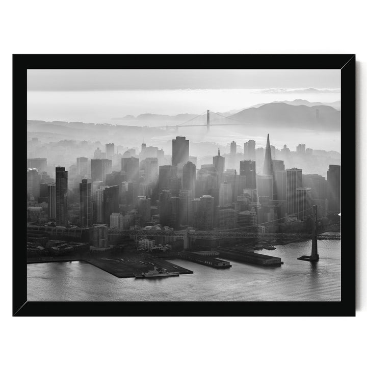 A black and white aerial view of the San Francisco skyline, with the Golden Gate Bridge and foggy mountains in the background.