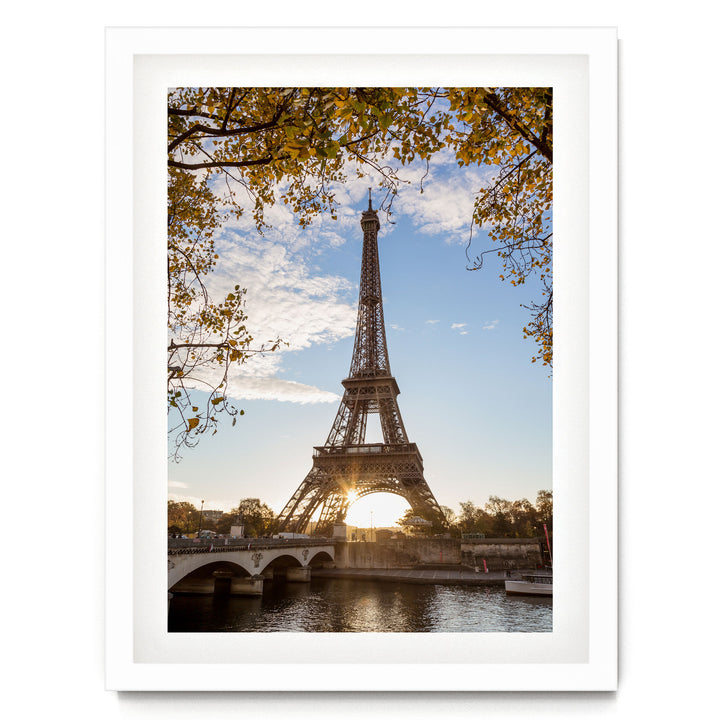 the Eiffel Tower in Paris, France, with a bridge and trees in the foreground, and the sun setting in the background.