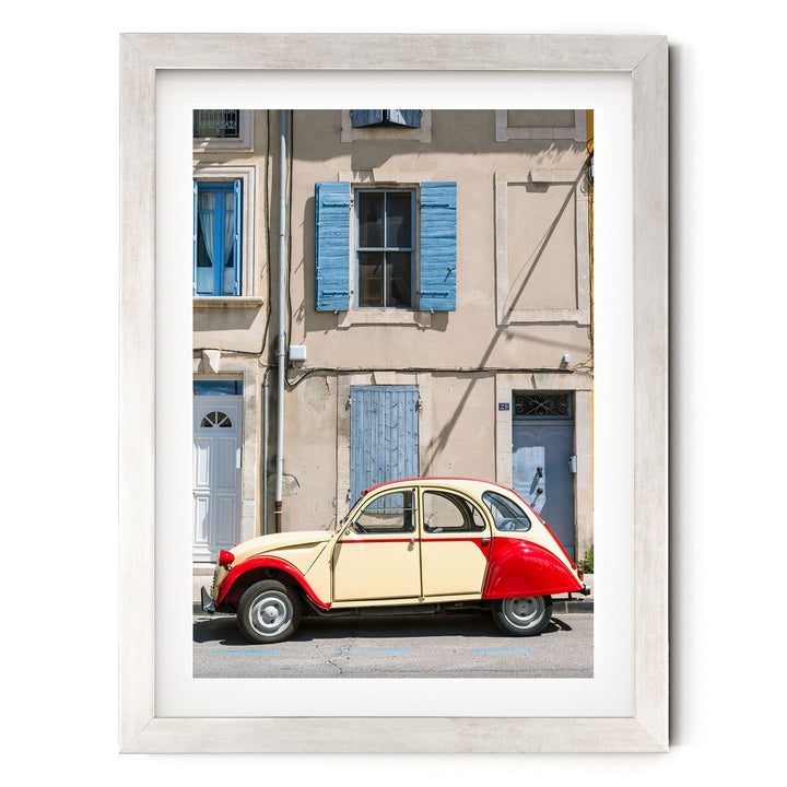 A vintage yellow and red car is parked on a street in front of a building with blue shutters and a white door.