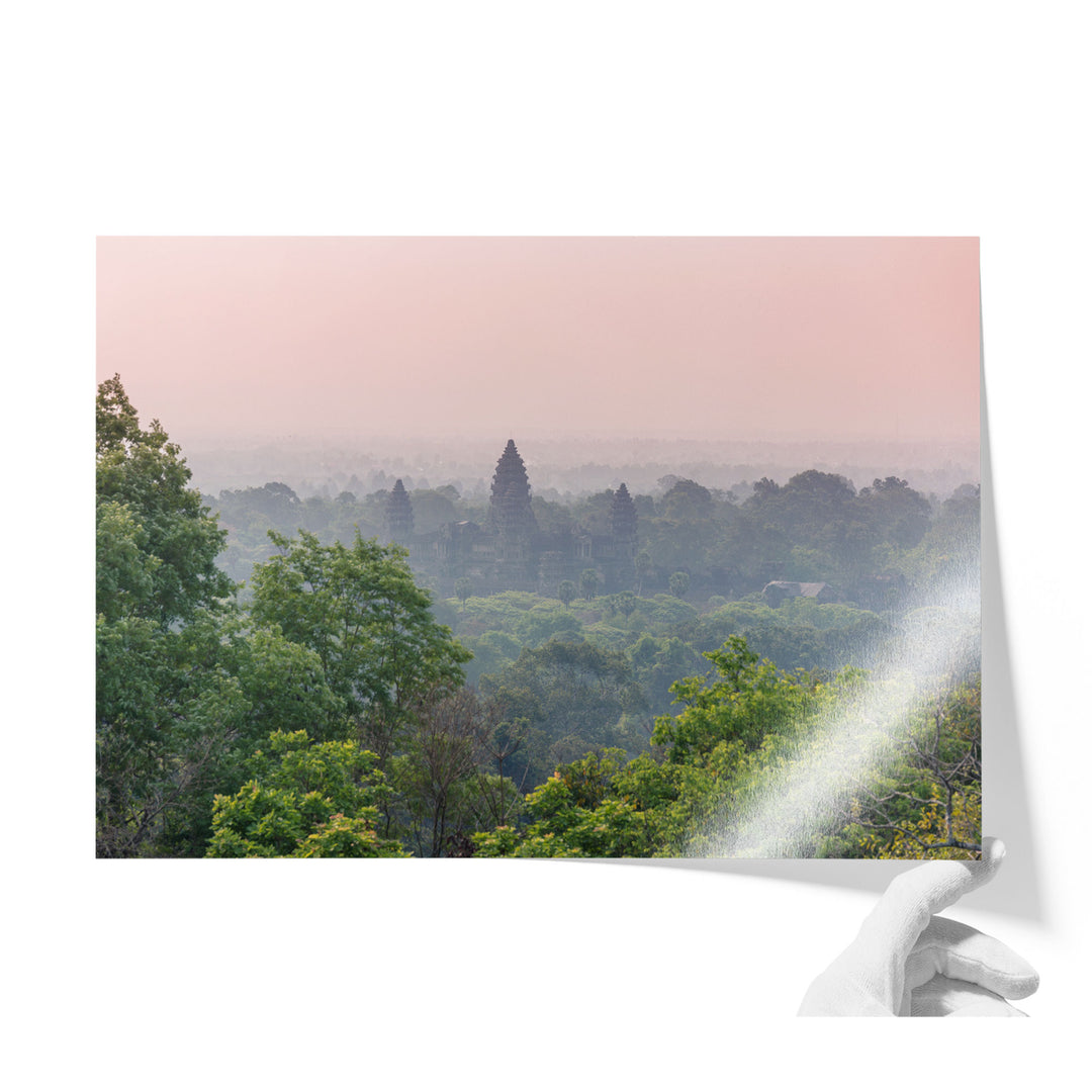 A hand is holding a piece of paper with a photograph of a lush, forested landscape with a temple visible in the distance.