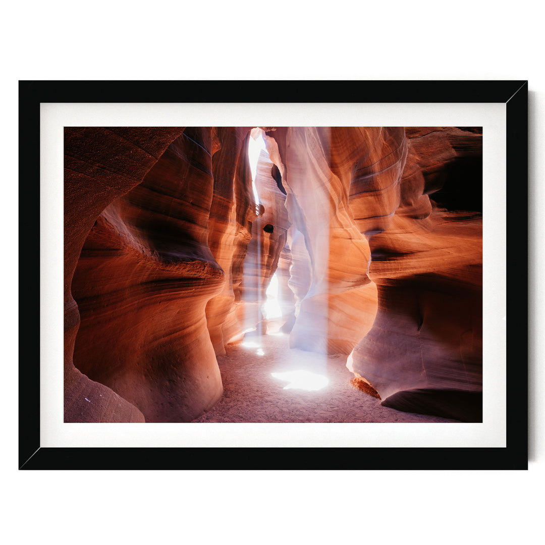 A framed photograph depicting a narrow, winding path through a canyon with a bright light shining through the rock formations.