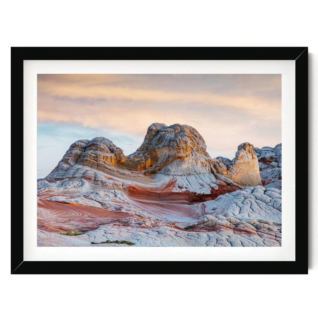 A framed image depicting a striking natural landscape with a large, multi-layered rock formation in the foreground, set against a vibrant sky with a gradient of orange and pink hues.