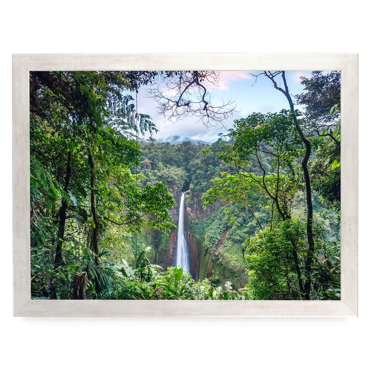 A lush, verdant forest with a towering waterfall cascading down the rocky cliff face, surrounded by dense foliage and a cloudy sky.
