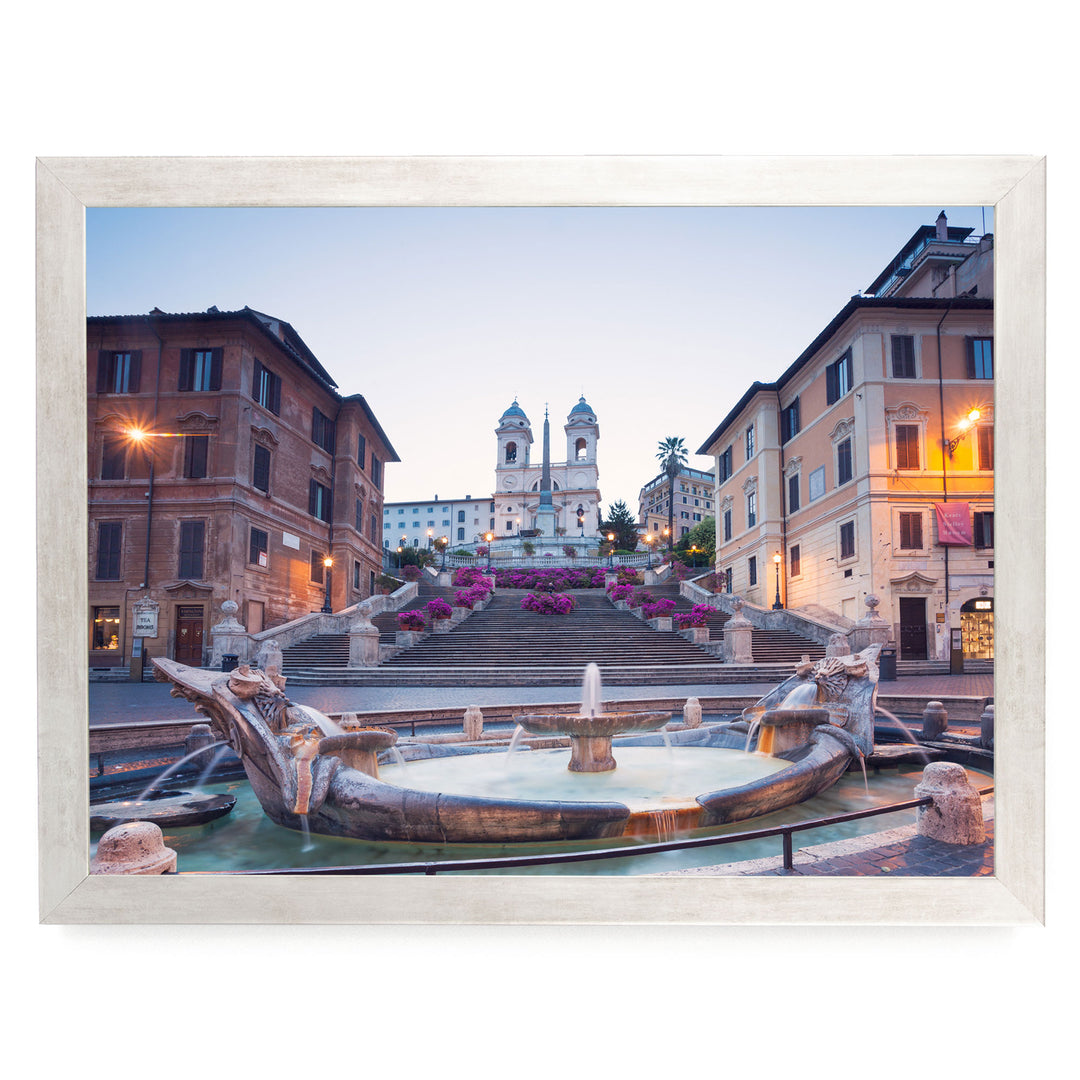 a picturesque scene of a fountain situated in a square, surrounded by ornate buildings and a church with two towers. The fountain is adorned with statues of mythical creatures, adding to the overall charm of the scene. The sky above is a beautiful shade of blue, providing a serene backdrop to the architectural marvel.