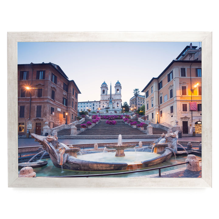 a picturesque scene of a fountain situated in a square, surrounded by ornate buildings and a church with two towers. The fountain is adorned with statues of mythical creatures, adding to the overall charm of the scene. The sky above is a beautiful shade of blue, providing a serene backdrop to the architectural marvel.