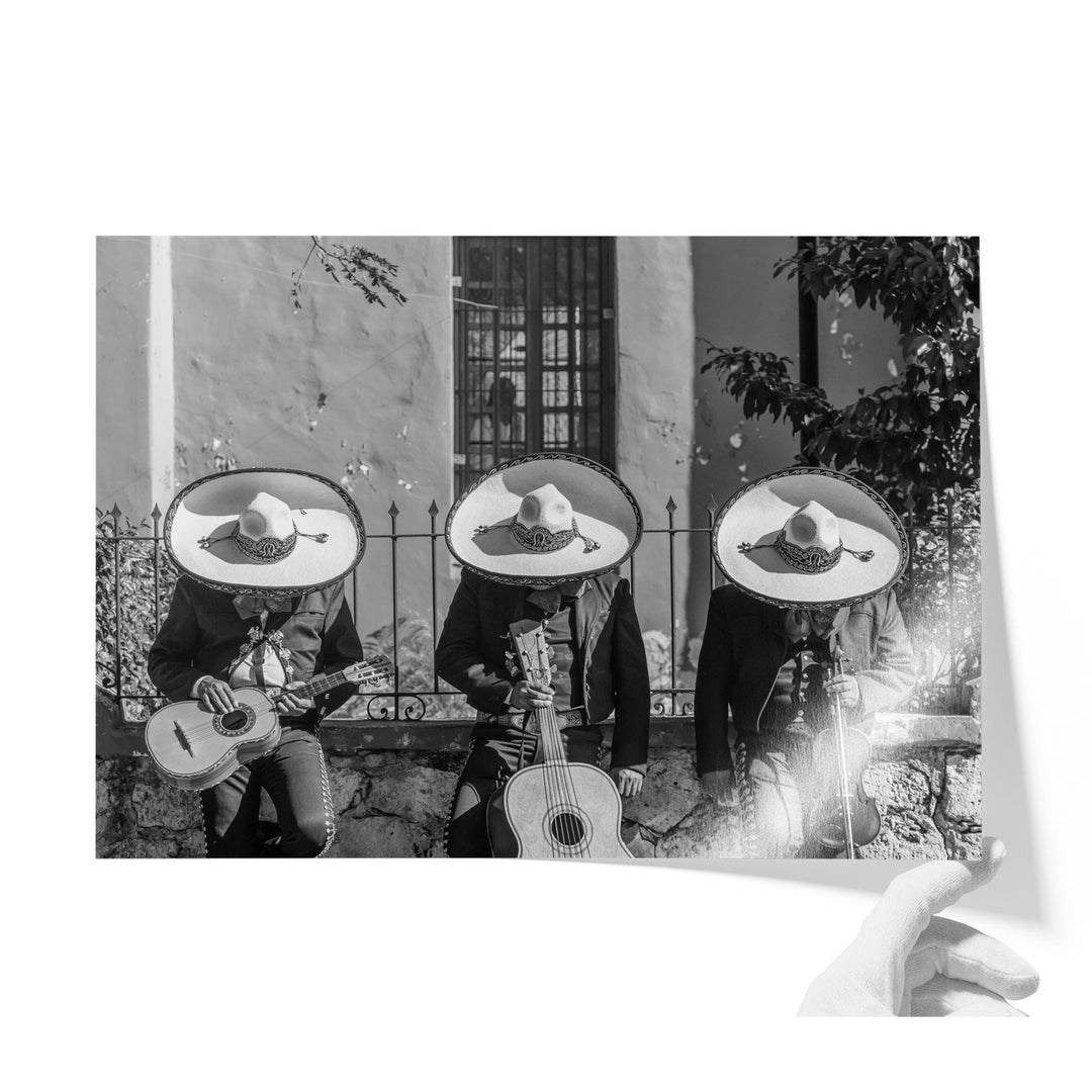 Three musicians wearing sombreros and playing guitar, arranged in a row, with a hand pointing towards the bottom right corner of the image.