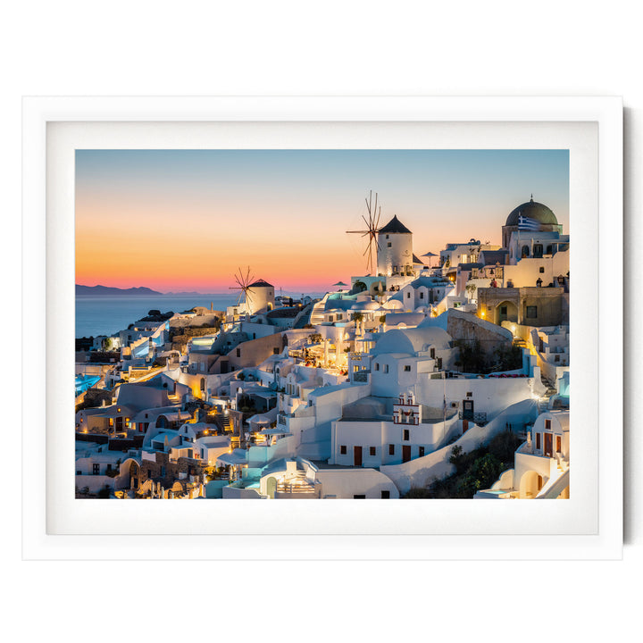 a picturesque coastal town with white buildings, windmills, and a stunning sunset over the water.