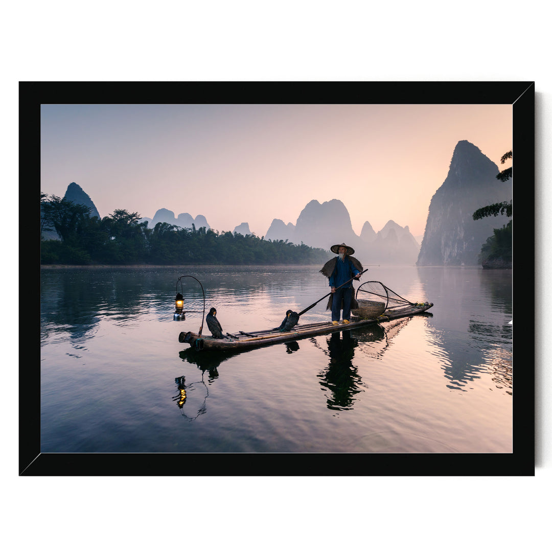 A person in a blue shirt and hat is standing on a long wooden boat, paddling through a serene lake at sunset.