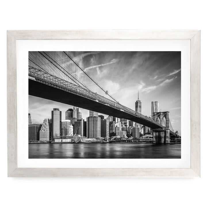 A black and white photograph of the Brooklyn Bridge spanning the East River, with the city skyline of New York City visible in the background.