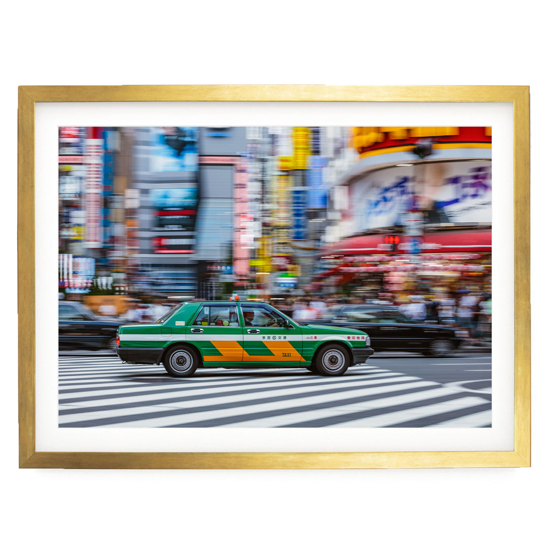 A green and yellow taxi cab is driving through a busy city street, with tall buildings and colorful signs in the background.