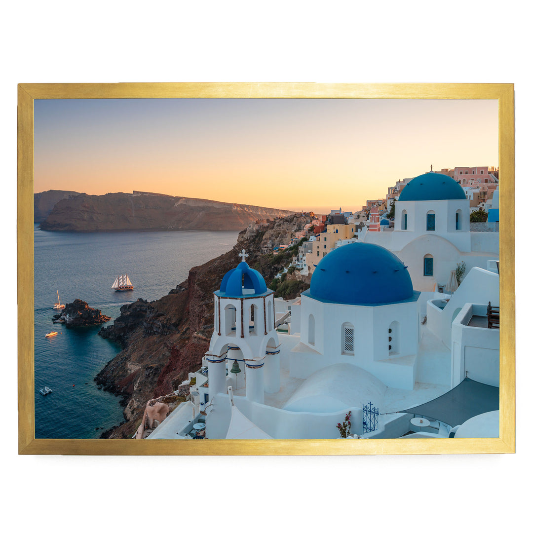 a picturesque coastal town with white buildings and blue domes, overlooking the ocean. The town is situated on a cliff, with a clear blue sky and a warm sunset in the background.