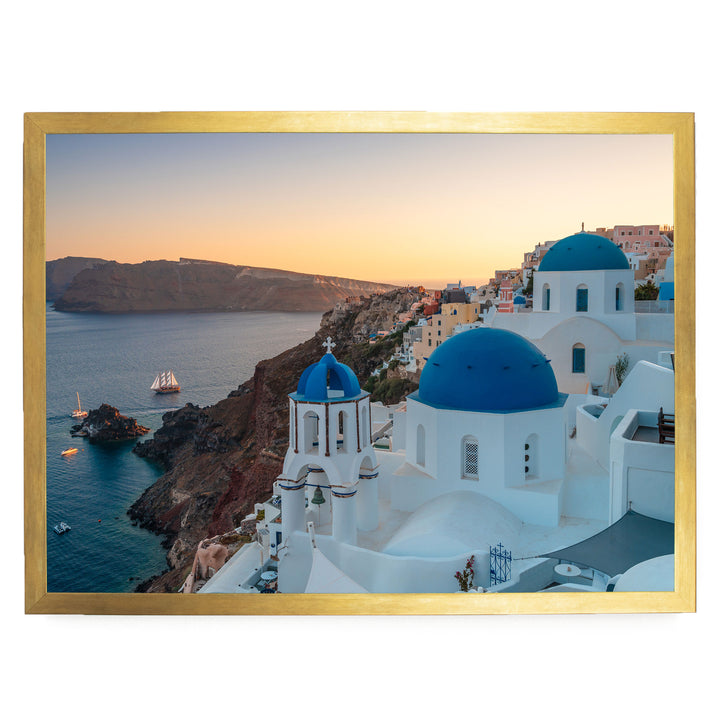 a picturesque coastal town with white buildings and blue domes, overlooking the ocean. The town is situated on a cliff, with a clear blue sky and a warm sunset in the background.
