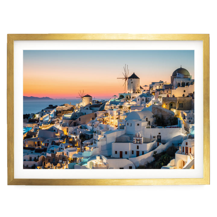a picturesque coastal town at sunset, with white buildings and windmills illuminated against a vibrant sky.