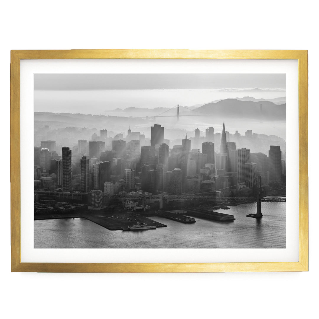 A black and white aerial view of a densely populated city skyline, with the Golden Gate Bridge visible in the distance.