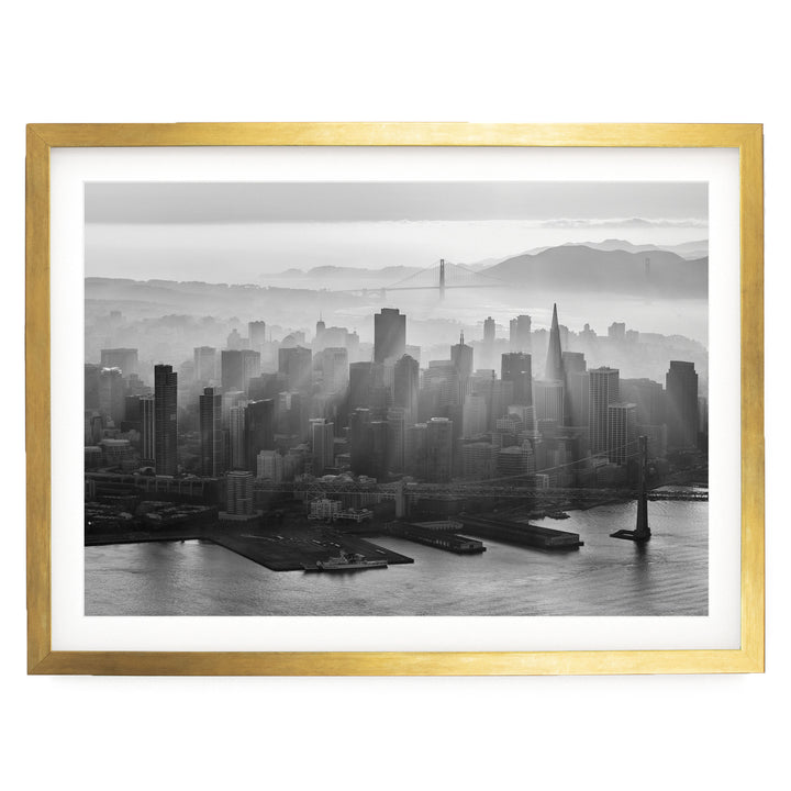A black and white aerial view of a densely populated city skyline, with the Golden Gate Bridge visible in the distance.