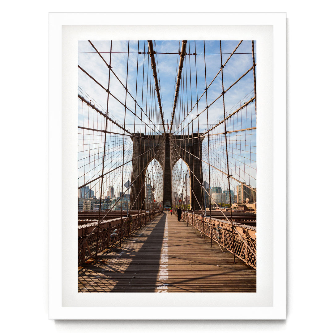 the iconic Brooklyn Bridge, with its distinctive arches and cables stretching across the frame, leading to the city skyline in the distance.