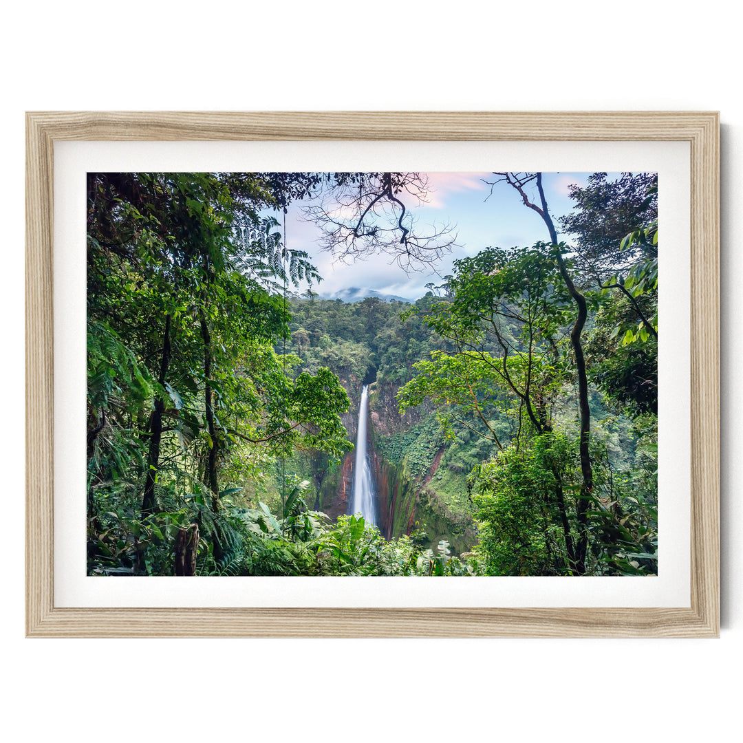 A lush, verdant forest with a towering waterfall cascading down the rocky cliff face, framed in a wooden frame.
