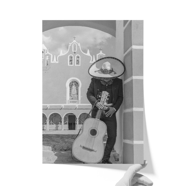 A person in a sombrero and traditional Mexican attire is playing a guitar in front of a building with arched windows and a cross on top.