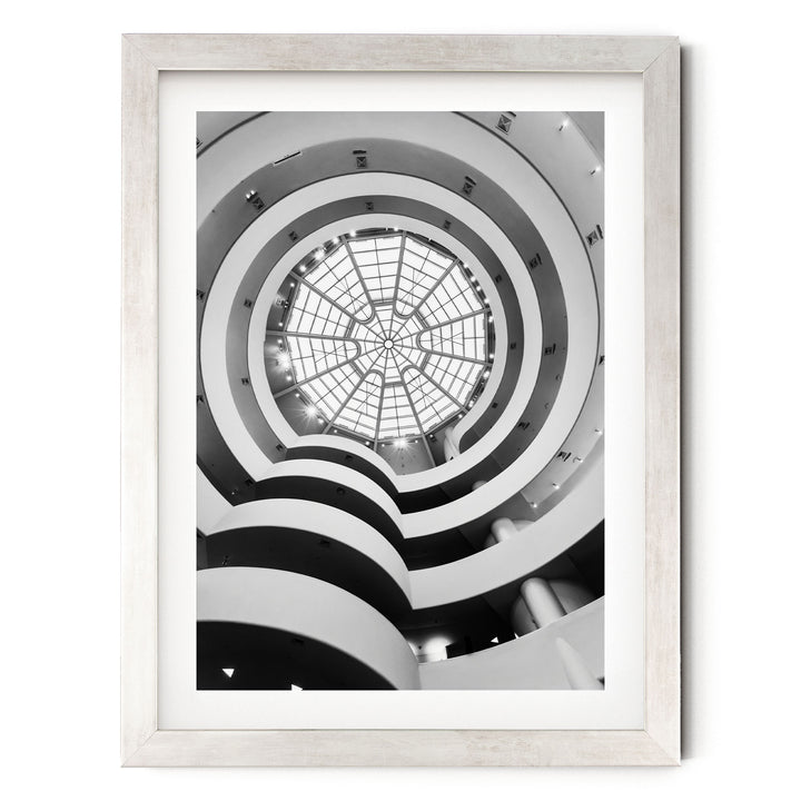 A black and white photograph of a spiral staircase with a large circular skylight at the top, creating a striking visual effect.