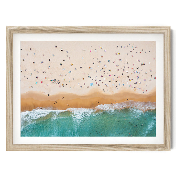 The image is a framed photograph depicting a crowded beach scene with people enjoying the sun, sand, and water.