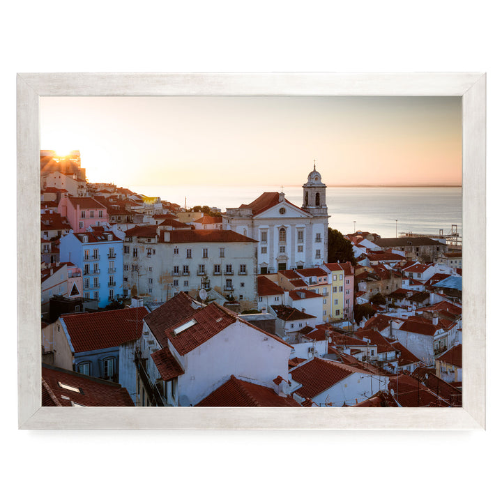 a picturesque town with a church and colorful buildings set against a backdrop of a sunset over the ocean.