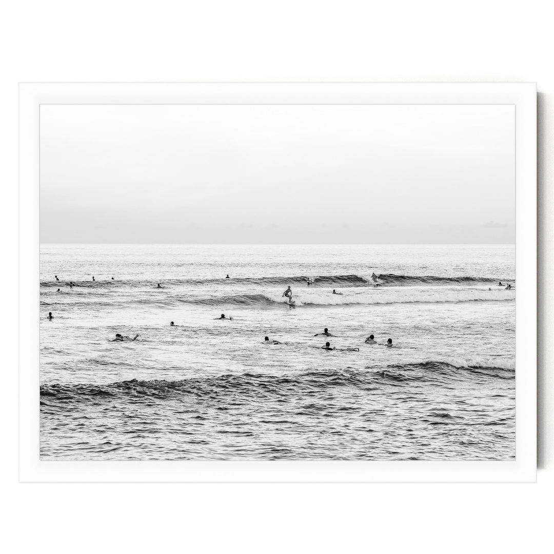 A black and white image of a group of people swimming and surfing in the ocean, with waves visible in the background.