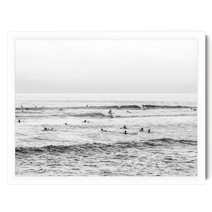 A black and white image of a group of people swimming and surfing in the ocean, with waves visible in the background.