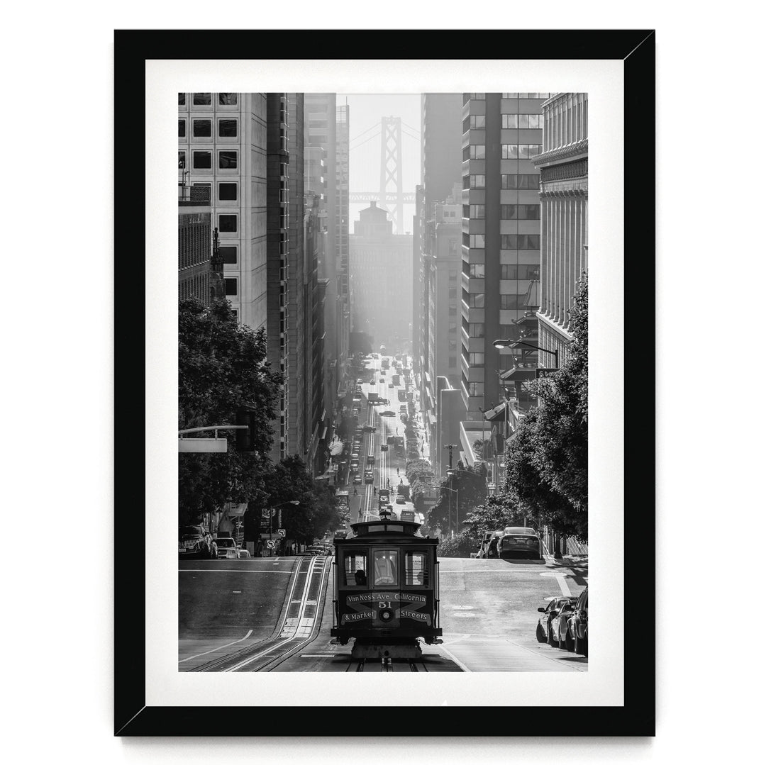 A black and white photograph of a trolley car traveling down a busy city street, surrounded by tall buildings and traffic.