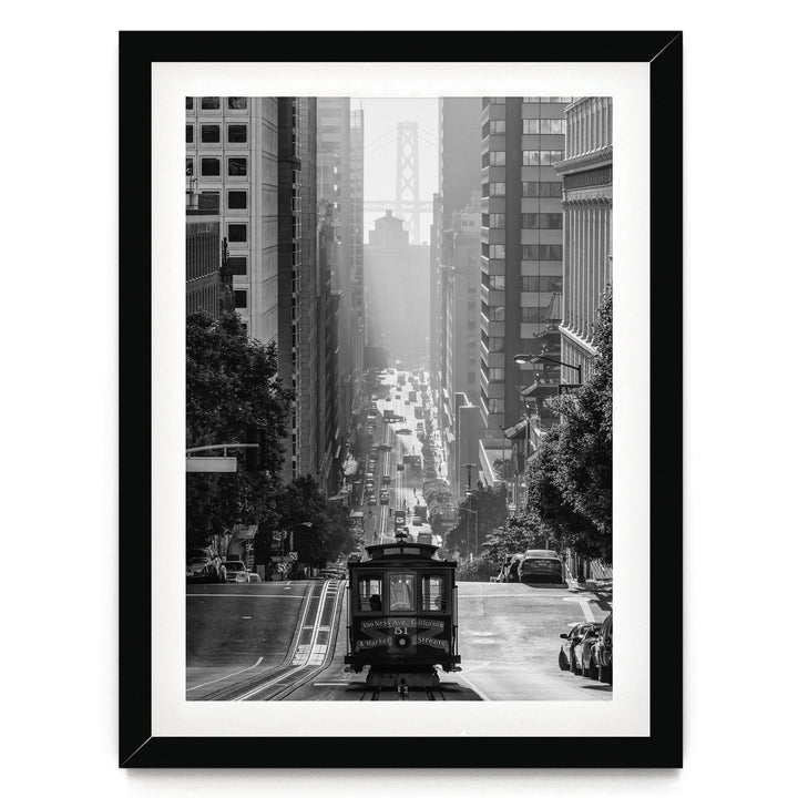 A black and white photograph of a trolley car traveling down a busy city street, surrounded by tall buildings and traffic.