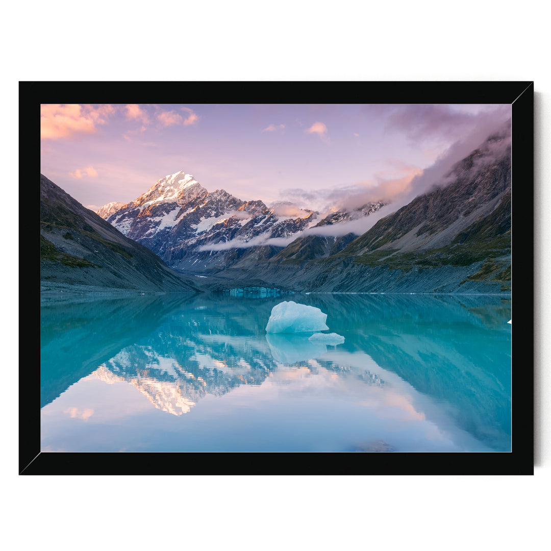 A breathtaking landscape featuring a serene lake with a large ice formation in the center, surrounded by majestic snow-capped mountains under a vibrant sky.