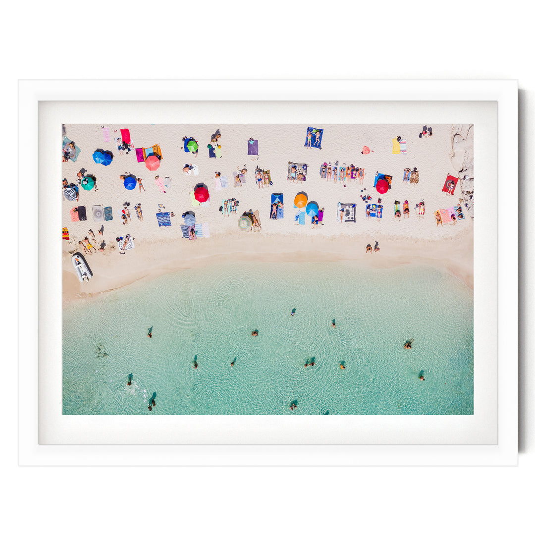a crowded beach with numerous people enjoying the sunny day, umbrellas, and towels spread across the sandy shore.