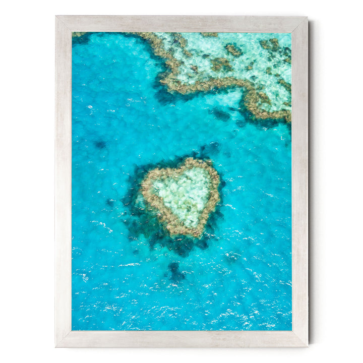 The image is a framed aerial view of a coral reef, showcasing the vibrant blue waters and the intricate coral formations.