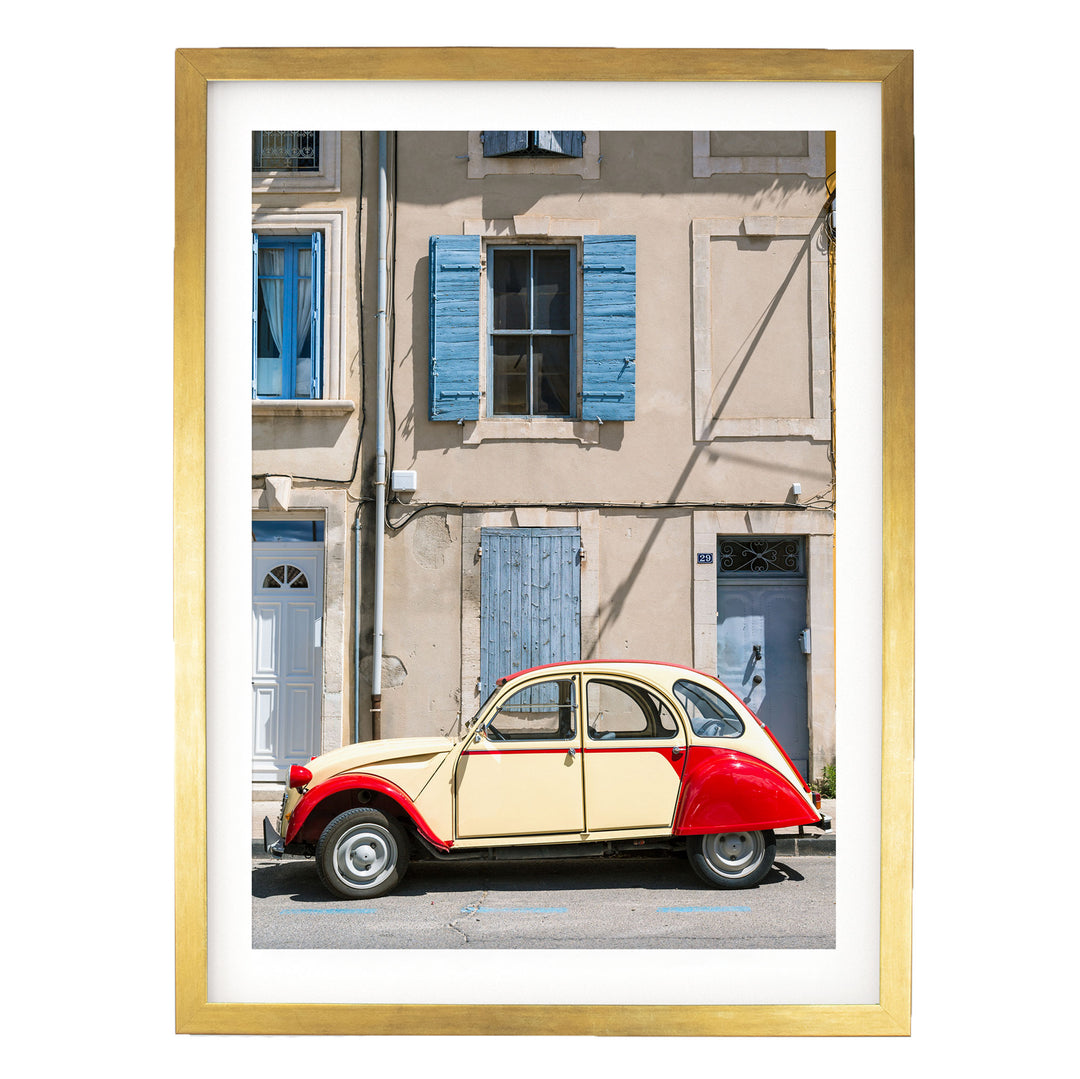 A vintage red and cream-colored car is parked on a street in front of a building with blue shutters and a white door.