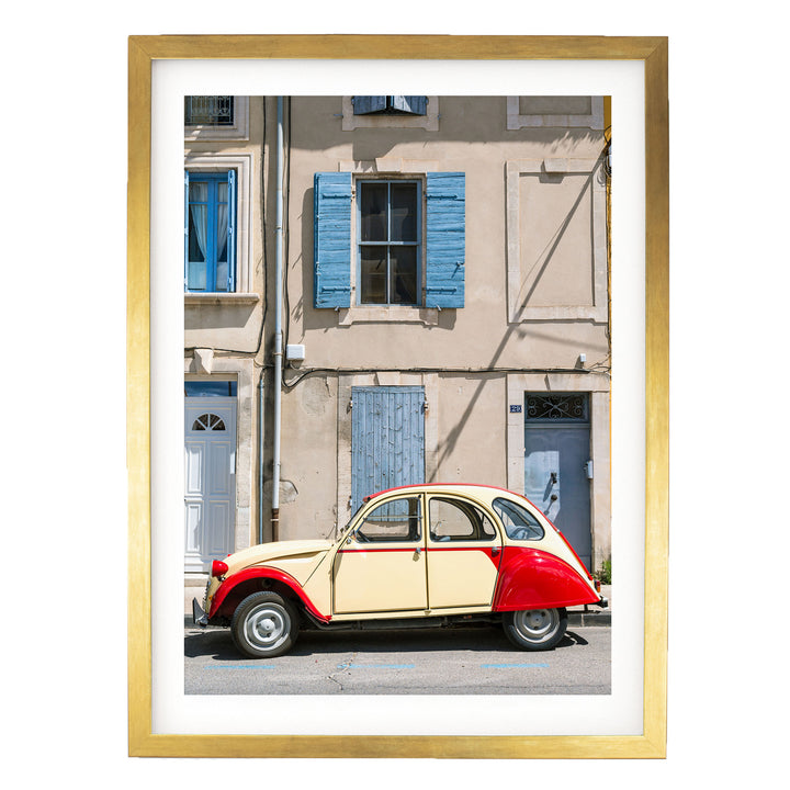 A vintage red and cream-colored car is parked on a street in front of a building with blue shutters and a white door.