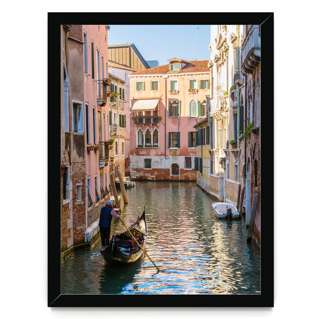 A gondolier navigates a traditional Venetian gondola through a picturesque canal, surrounded by colorful buildings and reflecting the clear blue sky.