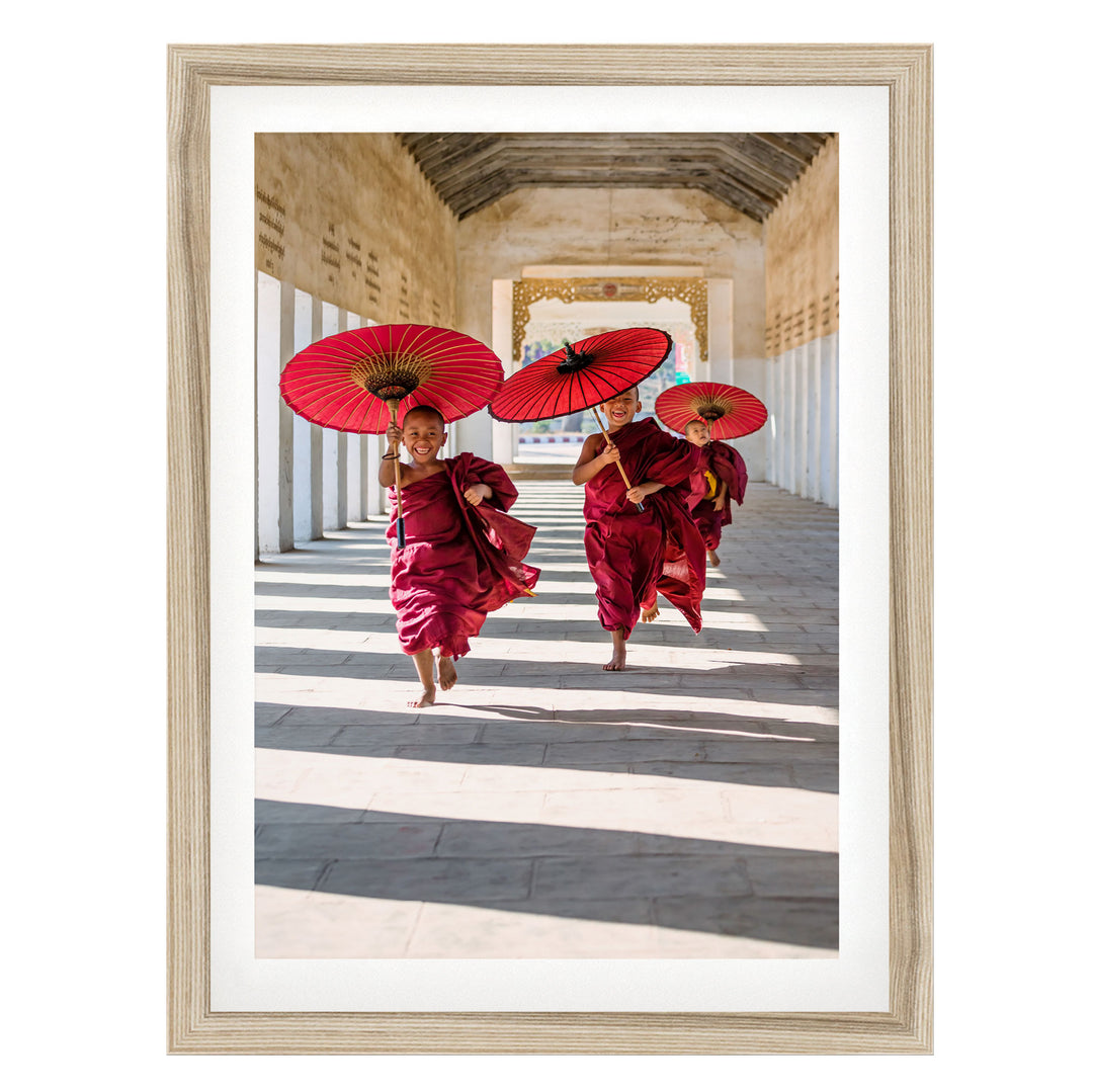 Two young monks in red robes are walking down a hallway, each holding a red umbrella.